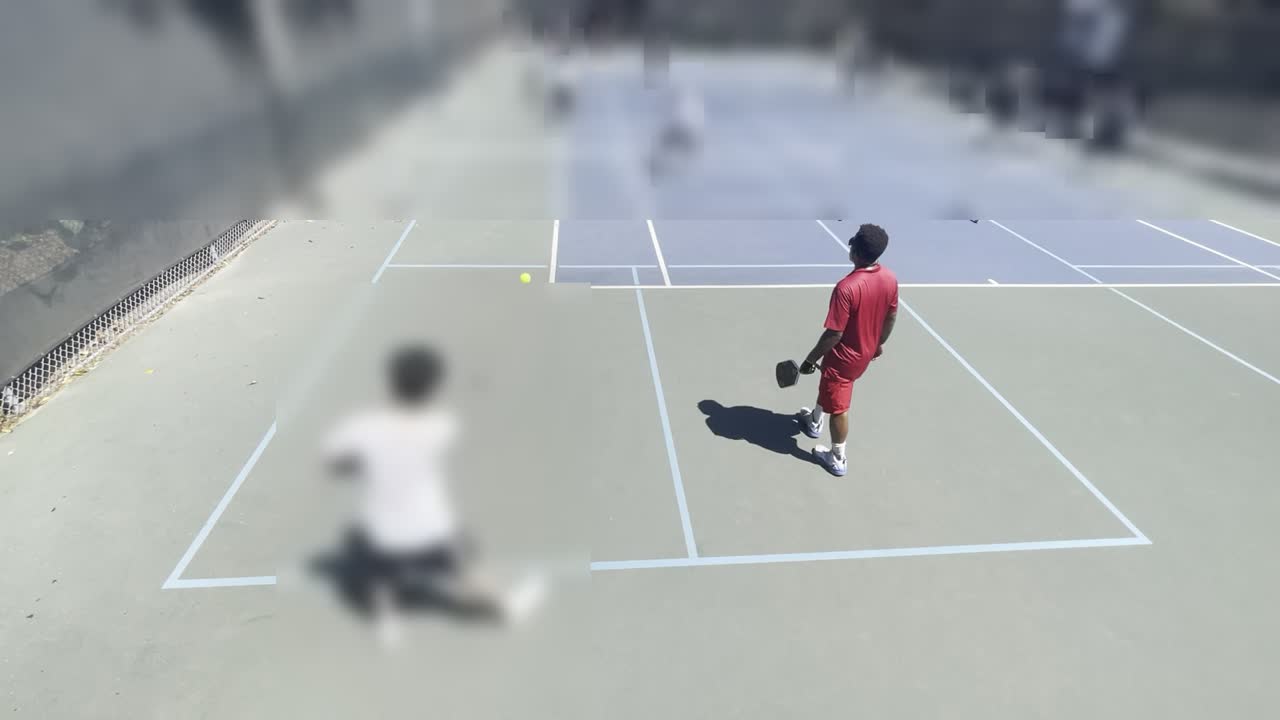 The analyzed player in a red shirt on the near court, filmed from behind the baseline; every other person in the frame is blurred.